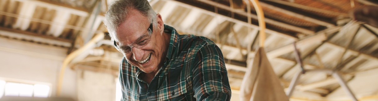 A senior man cutting wooden planks in a workshop.