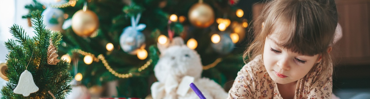 A girl writing a letter in front of a Christmas tree.
