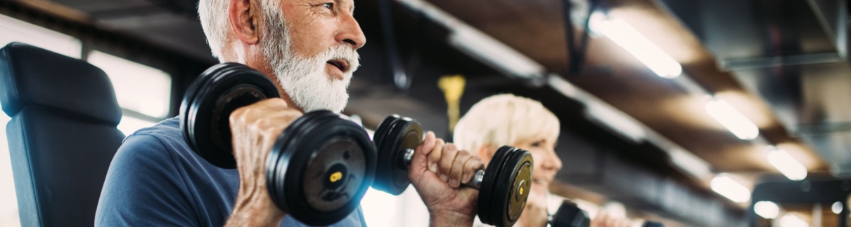 Two people in their 60s using weights in a gym.