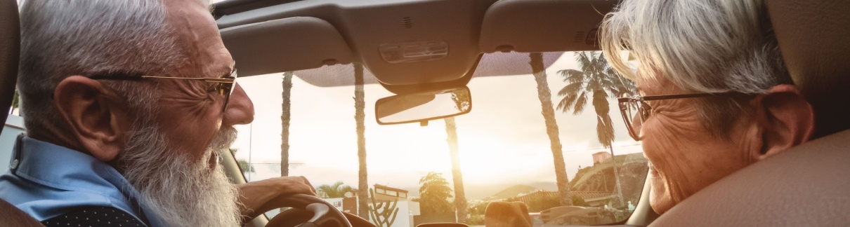 A happy older couple driving in a convertible car.