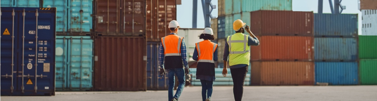 Workers walking through a shipping cargo container terminal depot.