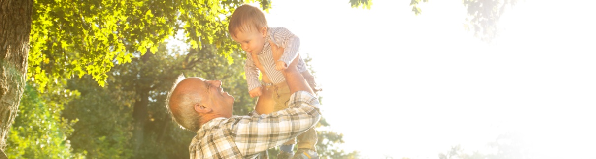A grandfather playing with his young grandson in a park.