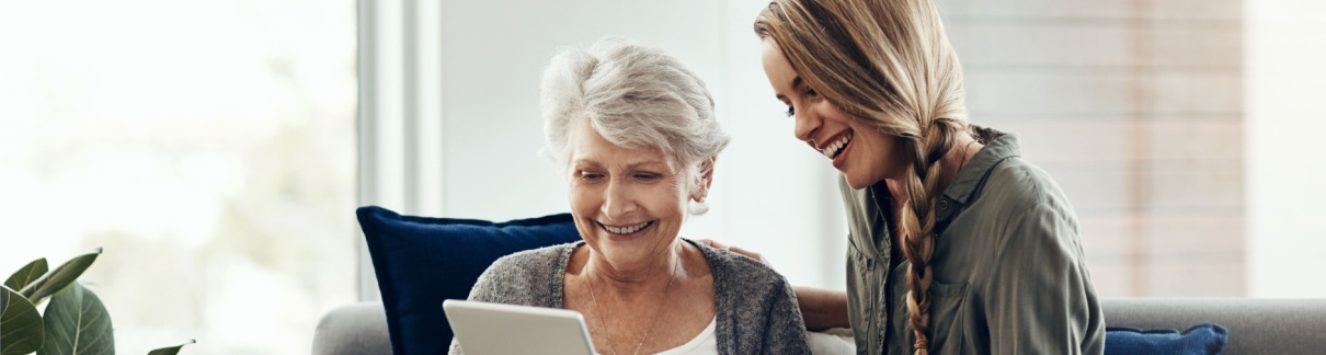 A woman showing her adult daughter something on a tablet.