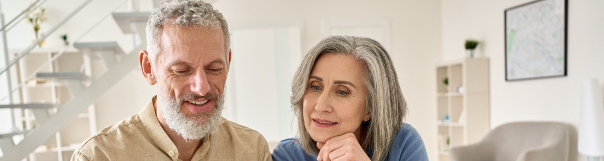 A senior couple sit at a laptop comparing multiple documents