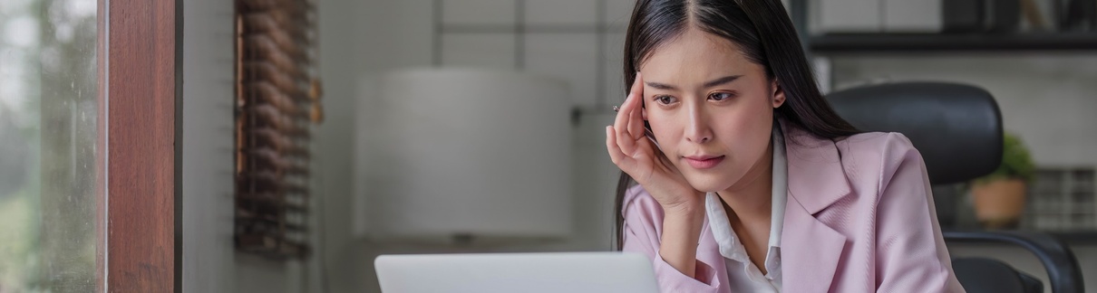 A woman at her computer, thinking carefully.