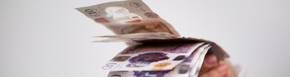 A hand holding UK bank notes.