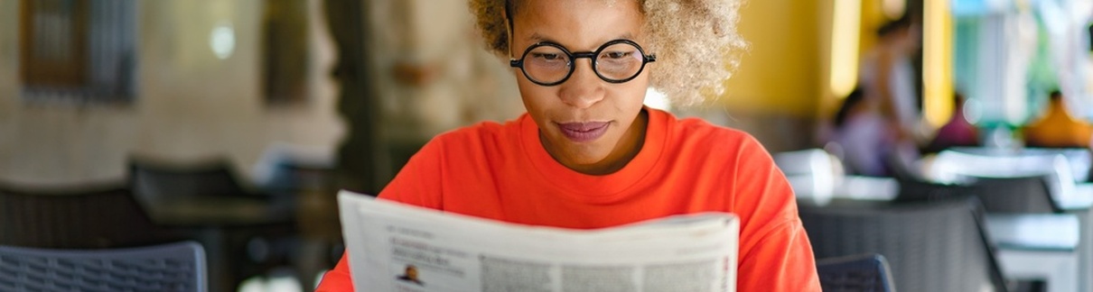 A woman reading a newspaper in a café.